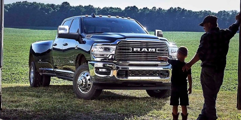 Black RAM heavy-duty truck parked on a farm with people standing beside it near open fields