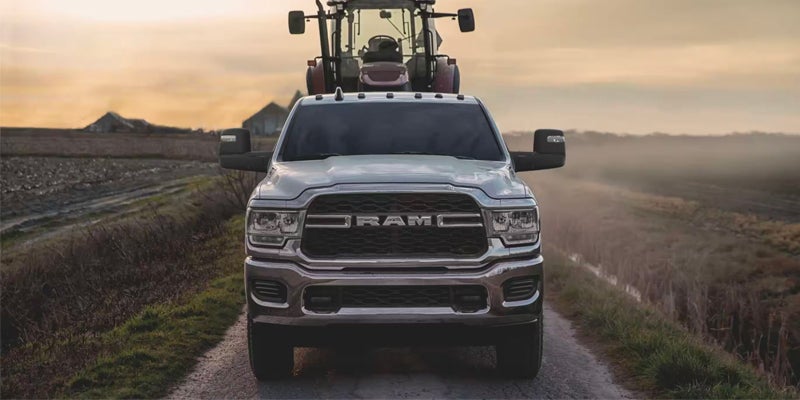 Front view of a silver RAM pickup truck driving on a narrow rural road with farm fields on both sides