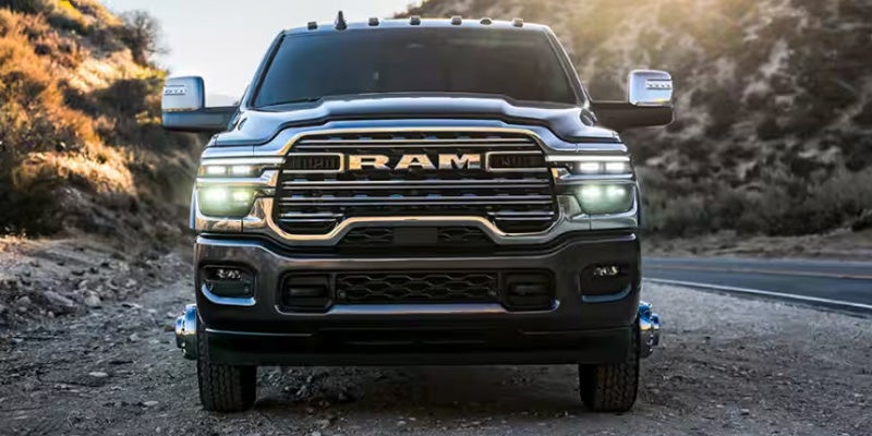 Front view of a black RAM heavy-duty pickup truck parked on a rugged roadside with headlights illuminated