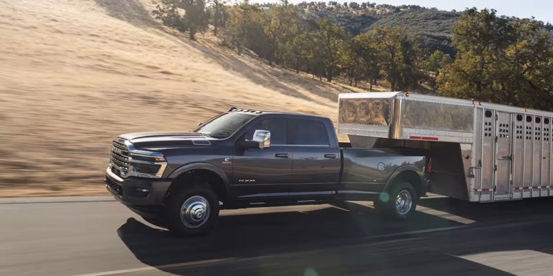 RAM heavy-duty dually truck towing a livestock trailer through a countryside landscape