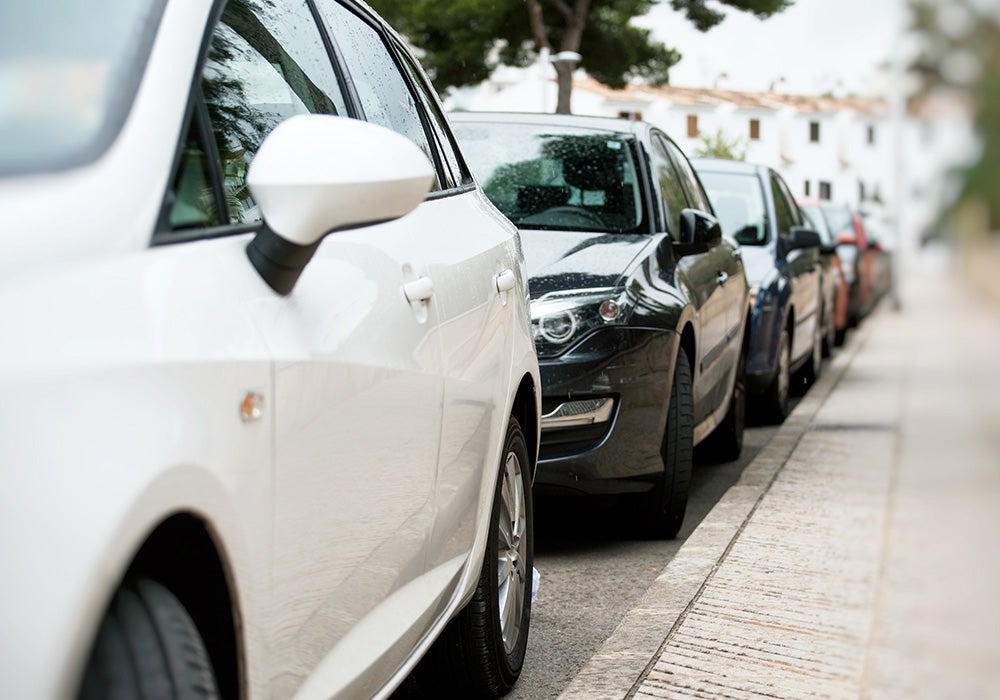 Line of cars parked along a curb, with a white car in the foreground